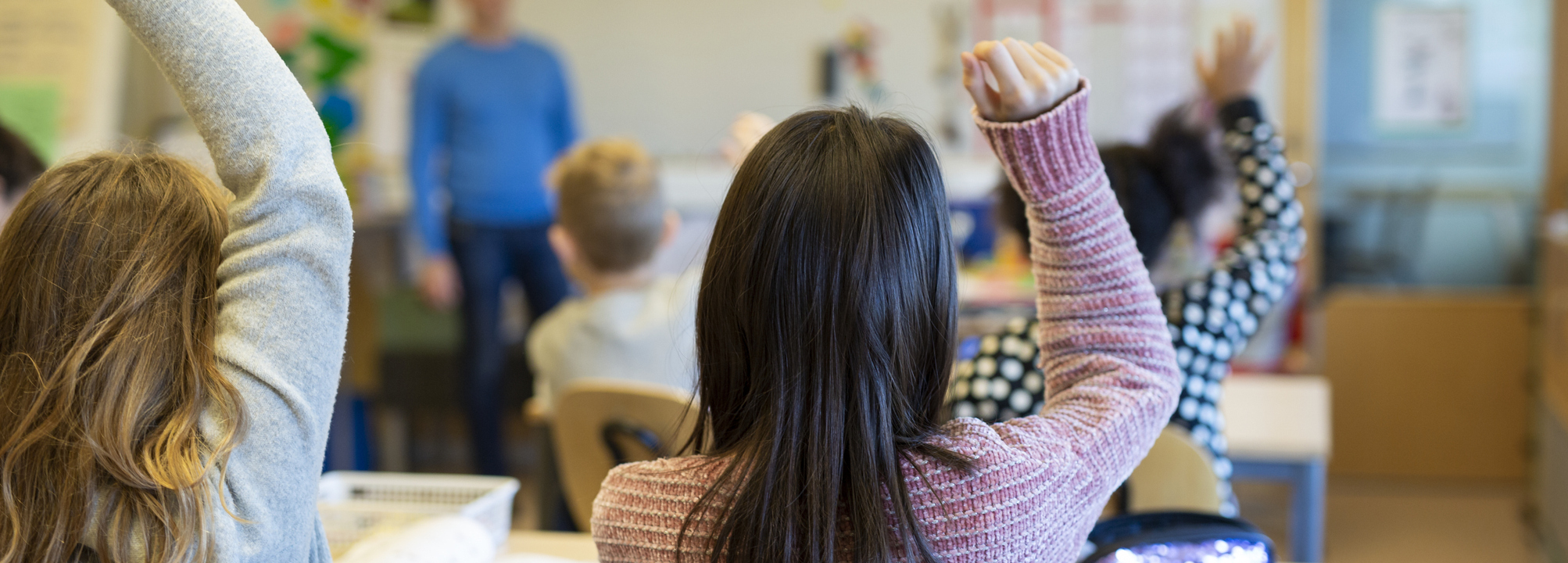 En grupp barn som räcker upp händerna i ett klassrum.